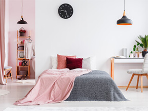 Modern bedroom with white and pink walls, pink and grey throw rugs and study desk with black clock